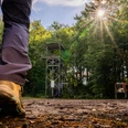 Bergbauweg Ein Wanderer nähert sich einem Aussichtsturm im Wald, während die Sonne durch die Bäume scheint.
