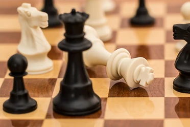 Schachturnier Schachbrett mit umgefallener weißer Königfigur neben schwarzen Spielfiguren nach einer Partie