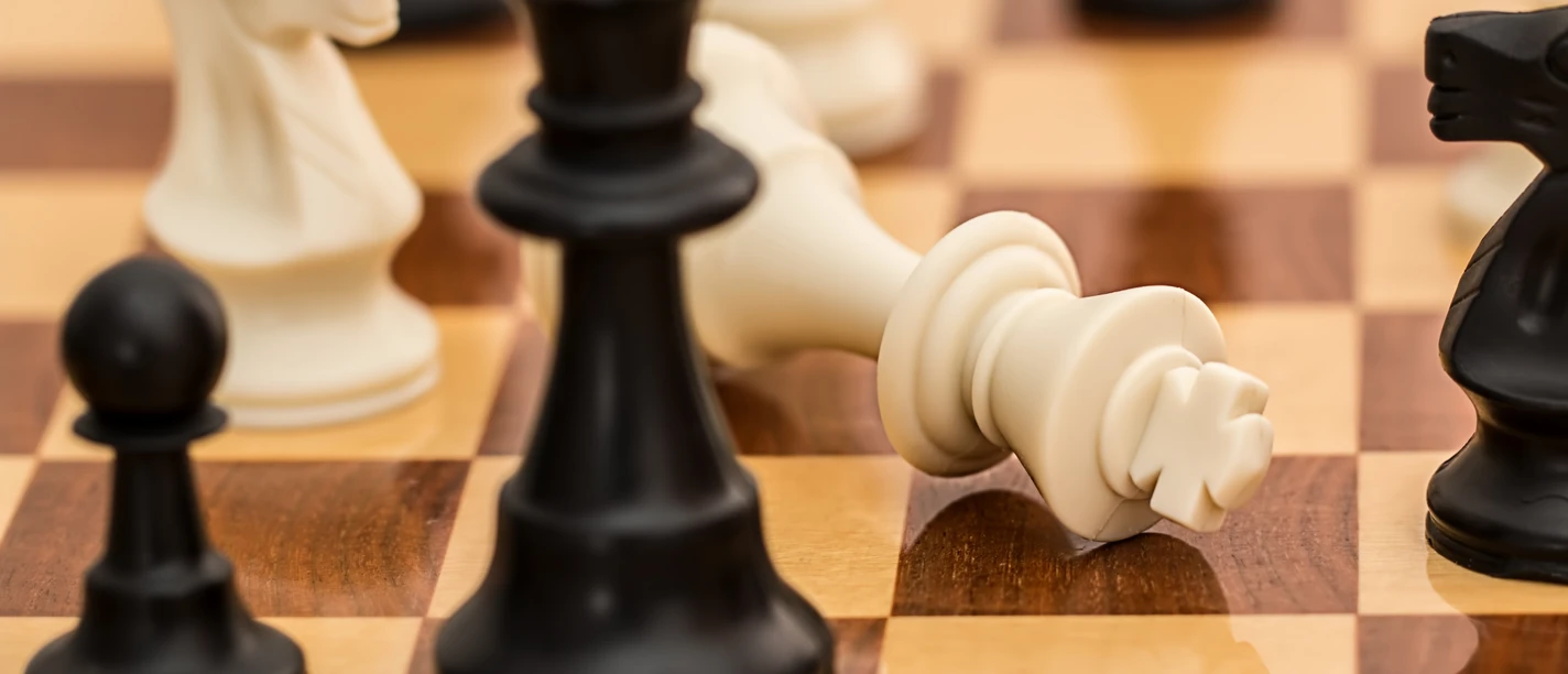 Schachbrett mit umgefallener weißer Königfigur neben schwarzen Spielfiguren nach einer Partie