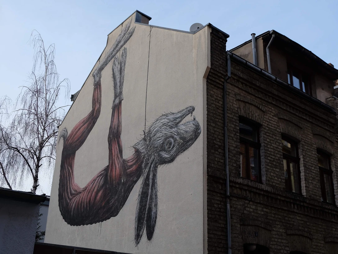 Mural Ein beeindruckendes Mural zeigt detailreich einen großen Hasen, der an einer Wand hängend abgebildet ist, dies verleiht der Gebäudefassade eine einzigartige Note.An impressive mural depicts a large rabbit hanging on a wall in great detail, giving the building façade a unique touch.