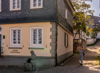 Altes Stadthaus Wipperfürth Ablasshäuschen in Wipperfürth mit traditioneller Architektur und einer Frau, die ein Mobiltelefon benutzt.