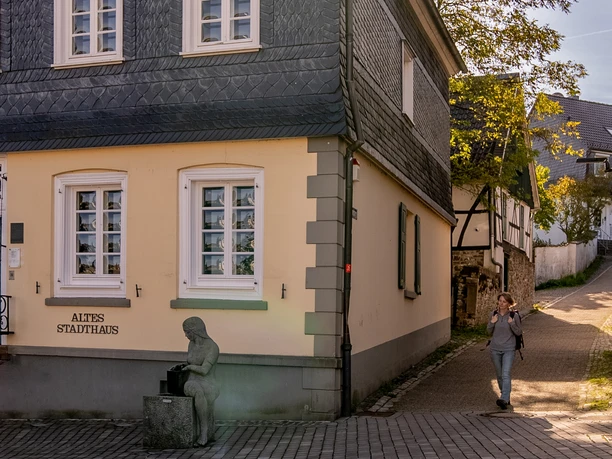 Altes Stadthaus Wipperfürth Ablasshäuschen in Wipperfürth mit traditioneller Architektur und einer Frau, die ein Mobiltelefon benutzt.