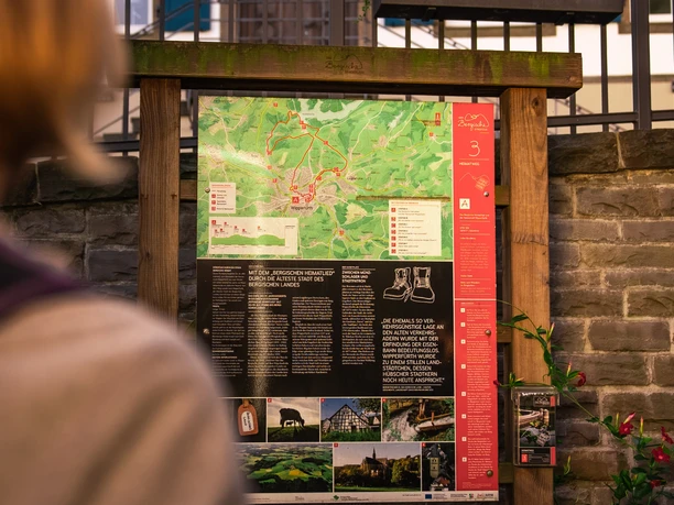 Infotafel am Heimatweg Eine Frau steht vor einer Infotafel mit Wanderkarten und Informationen, umgeben von grüner Natur.