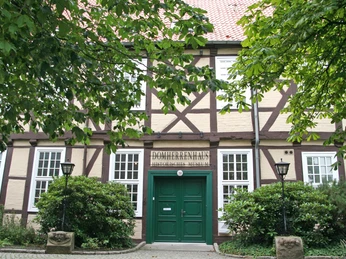 Museum Domherrenhaus Fachwerkhaus mit grünem Eingang, großen Fenstern, umgeben von Bäumen und Laternen; Museumsschild.Half-timbered house with green entrance, large windows, surrounded by trees and lanterns; museum sign.Bindingsværkshus med grønt indgangsparti, store vinduer, omgivet af træer og lanterner; museumsskilt.Vakwerkhuis met groene ingang, grote ramen, omringd door bomen en lantaarns; uithangbord van het museum.