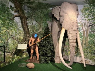 A prehistoric man with a spear stands next to an impressive replica of a mammoth in the museum.