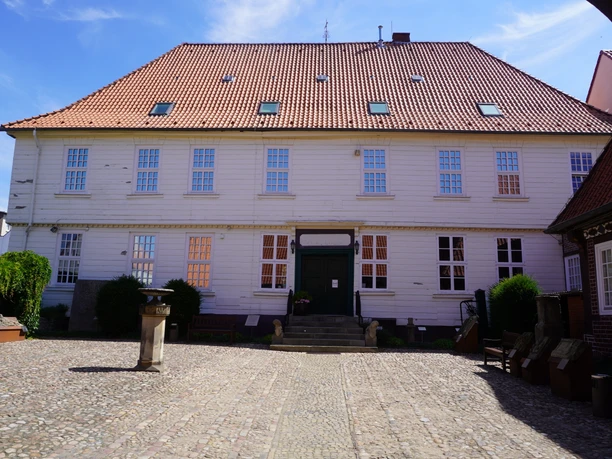 Historic building with red tiled roof and white façade, surrounded by a paved courtyard.