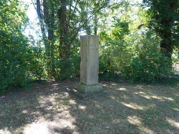 Bornemacher Stele Steinstele umgeben von Bäumen in einem schattigen Bereich, aufgestellt auf einem grünen Rasen.