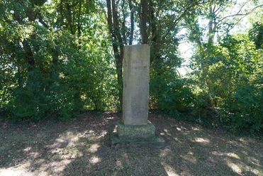 Bornemacher Stele Stele aus grauem Stein in Waldlichtung, umgeben von grünen Bäumen bei Tageslicht, steht ruhig.