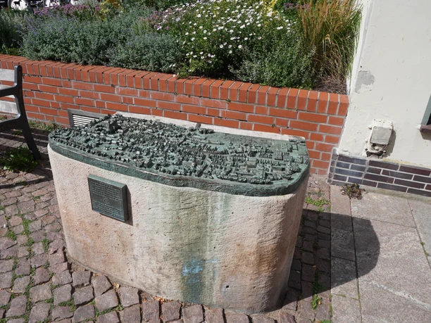 Stadtmodell Verden Detailliertes Bronzemodell der Altstadt Verden auf einem Steinsockel, umgeben von Blumenbeet.