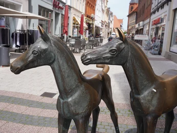 Skulptur Fohlengruppe Verden Bronzeskulptur von drei jungen Pferden in einer Einkaufsstraße in Verden, umgeben von Geschäften.