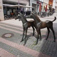 Bronzeskulptur zweier Fohlen in einer belebten Fußgängerzone von Verden mit Geschäften im Hintergrund.