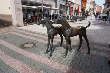 Skulptur Fohlengruppe Verden Bronzeskulptur zweier Fohlen in einer belebten Fußgängerzone von Verden mit Geschäften im Hintergrund.