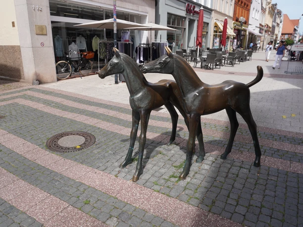 Skulptur Fohlengruppe Verden Bronzeskulptur zweier Fohlen in einer belebten Fußgängerzone von Verden mit Geschäften im Hintergrund.