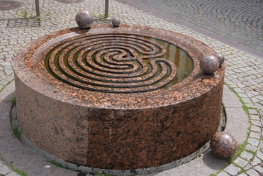 Der Gezeitenbrunnen in Verden ist ein runder, spiralförmiger Brunnen aus rötlichem Granit mit Kugeln.