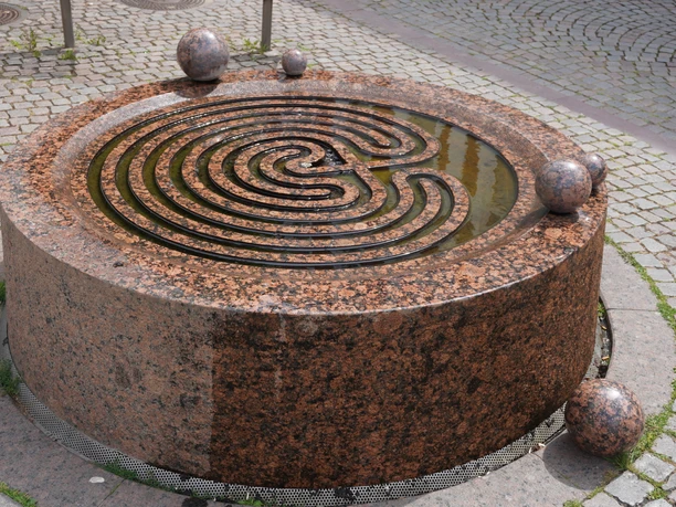 Der Gezeitenbrunnen in Verden ist ein runder, spiralförmiger Brunnen aus rötlichem Granit mit Kugeln.