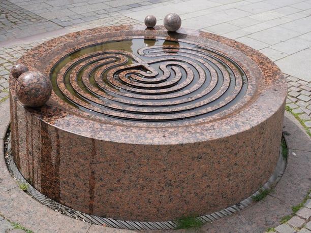 Ein kunstvoll gestalteter Gezeitenbrunnen aus rotem Granit mit spiralförmigen Wasserrinnen.