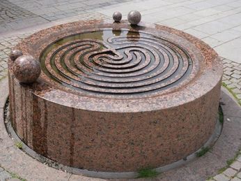Gezeitenbrunnen Verden Ein kunstvoll gestalteter Gezeitenbrunnen aus rotem Granit mit spiralförmigen Wasserrinnen.