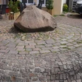 Großer, glattpolierter Stein auf einem Pflasterkreismuster, umgeben von kleinen Sitzgelegenheiten.