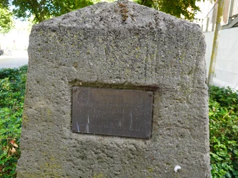 Ein Gedenkstein mit einer Metallplakette, umgeben von grünen Büschen, erinnert an Luther.