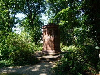 Backsteindenkmal mit runden Reliefs, umgeben von Bäumen im Bürgerpark Verden als Mahnmal für Vertreibung.