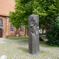 Mahnmal für die jüdischen Opfer Verden Mahnsäule aus dunklem Stein mit einer Reliefstruktur, umgeben von Bäumen und Backsteingebäude.