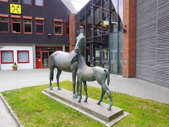 Die Skulptur einer Mutterstute mit Fohlen steht vor einem modernen Gebäude in Verden.