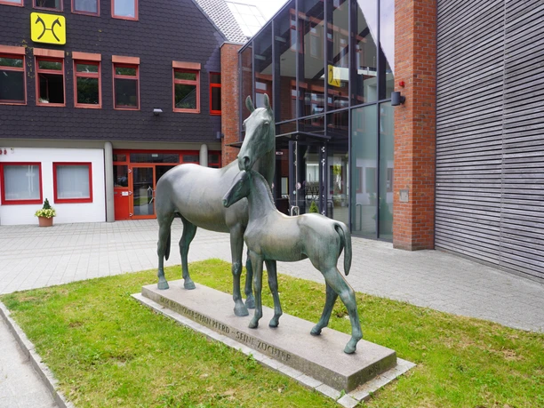 Skulptur Mutterstute mit Fohlen Verden Die Skulptur einer Mutterstute mit Fohlen steht vor einem modernen Gebäude in Verden.