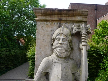 Wächterfiguren Verden Die historische Steinfigur eines alten Ritters mit Bart und Helm hält eine Axt im Grünen von Verden.