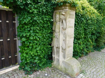 Steinfigur eines mittelalterlichen Wächters an einer mit Grün bewachsenen Mauer in Verden.