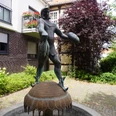 Brunnen mit einer Statue des Seeräubers Störtebeker in einer ruhigen Gartenanlage an einem gepflasterten Weg.