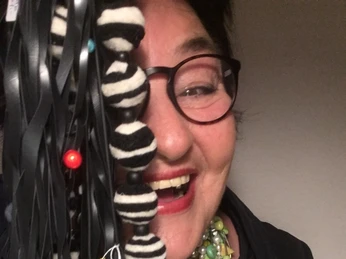 IMG_4047.jpg Frau mit schwarzer Brille und rotem Lippenstift zeigt eine Kette aus bunten Knöpfen und Bändern.