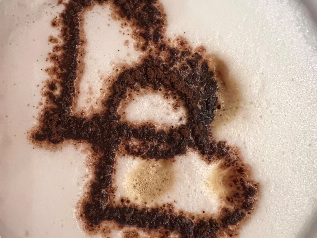 Kaffeetasse mit Herz-Motiv aus Kakaopulver auf dem Schaum einer cremigen Cappuccino-Oberfläche.