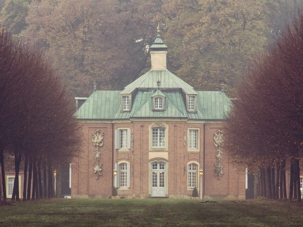 Schloss Clemenswerth im Herbst – Blick von Allee auf Zentralpavillon ©Emsland Tourismus GmbH.jpg Barockes Schloss Clemenswerth mit kupfergrünem Dach, umgeben von herbstlich kahler Baumallee im Nebel