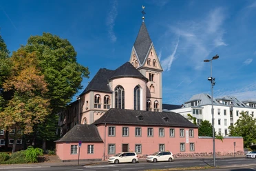 Sankt Maria in Lyskirchen St. Maria in Lyskirchen, rosa Kirche mit markantem Turm, umgeben von Bäumen und modernen Gebäuden.