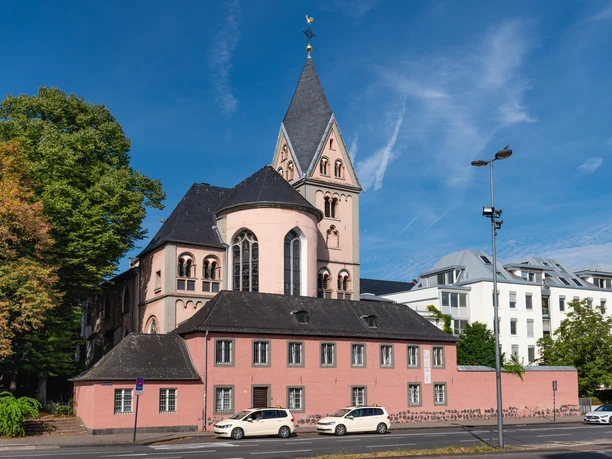 Sankt Maria in Lyskirchen St. Maria in Lyskirchen, rosa Kirche mit markantem Turm, umgeben von Bäumen und modernen Gebäuden.
