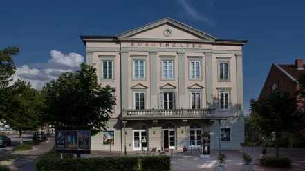 Burgtheater Aussenansicht (Jens Butz).jpg Das Burgtheater ist ein helles Gebäude. Es hat einen Balkon und eine Terrasse mit Sitzgelegenheiten.