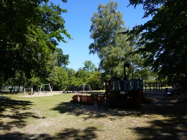 Playground in Verden's Bürgerpark, surrounded by trees, with various play structures and swings.