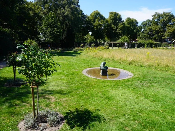 Rosengarten Verden Runde Brunnenskulptur umgeben von grünem Rasen und Bäumen im Rosengarten Verden bei sonnigem Wetter.