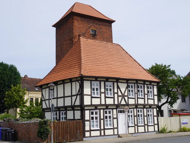 Historischer Fachwerkbau mit rotem Ziegeldach und Wehrturm in Verden, umgeben von grüner Umgebung.