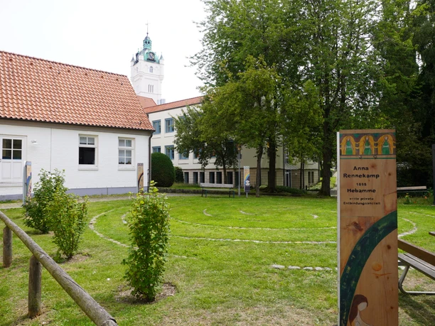 Spiralförmiges Labyrinth mit Wegmarkierungen auf einem gepflegten Rasen, umgeben von Gebäuden und Bäumen.