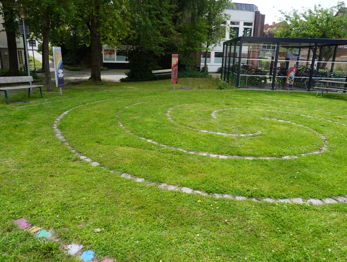 Spirallabyrinth Verden Spiralförmiges Labyrinth auf einer grünen Wiese, umgeben von Schildern und Bäumen in Verden.
