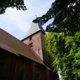 St. Andreaskirche Backsteinkirche mit hohem Turm und spitzem Dach, umgeben von grünen Bäumen, vor blauem Himmel.