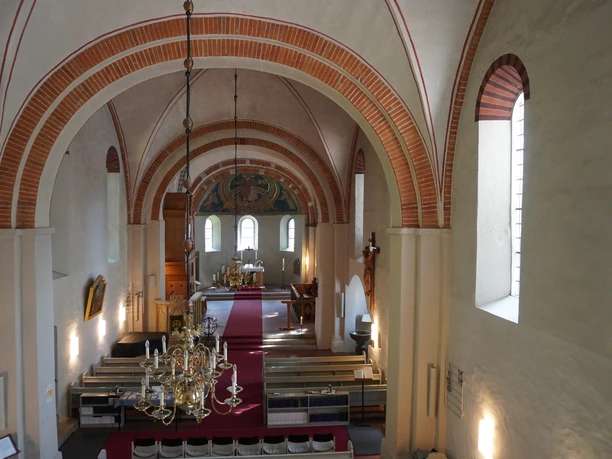 St. Andreaskirche Kircheninnenraum mit roten Backsteinbögen, hellem Mauerwerk, einem Altar und hölzernen Sitzbänken.