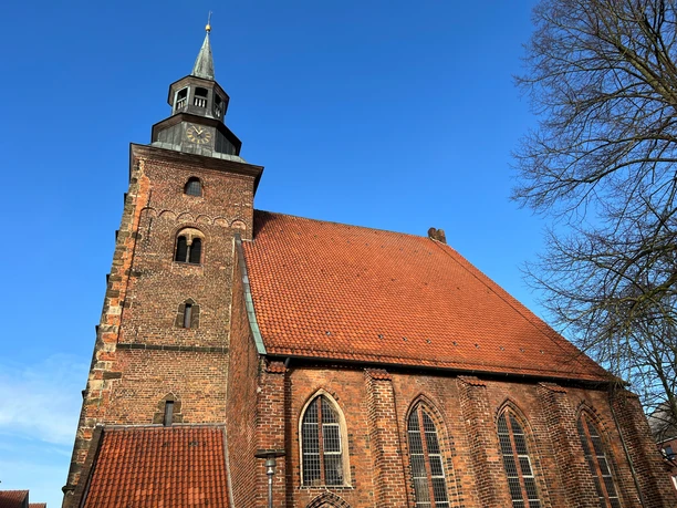 St. Johanniskirche Backsteinkirche mit rotem Ziegeldach, gotischen Fenstern und markantem Turm unter blauem Himmel.