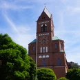 St. Josefkirche Verden Backsteinkirche mit grünem Dach, Glockenturm und strahlend blauem Himmel, umgeben von Bäumen.