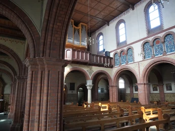 Ein lichtdurchflutetes Kirchenschiff der St. Josefkirche mit Bänken und einer beeindruckenden Orgel auf der Empore.