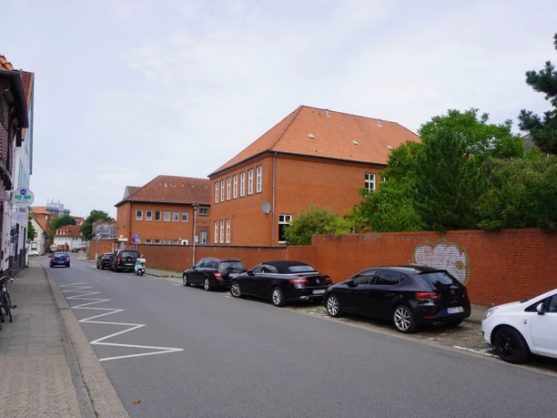 Amtsgericht mit Backsteinfassade, umgeben von geparkten Autos und Bäumen an einer ruhigen Straße.