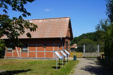 Storchenpflegestation in Verden mit Fachwerkgebäude, Infotafeln und grünem Umfeld unter blauem Himmel.