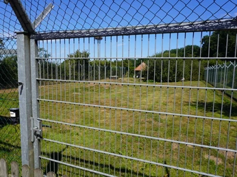 Ein weitläufiges, begrüntes Gehege mit Drahtzaun und blauem Himmel, geeignet für Vogelpflege.