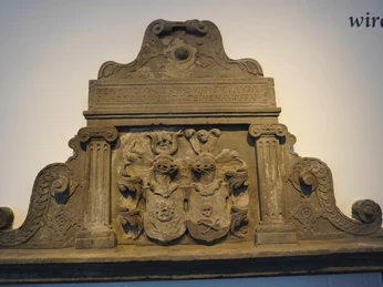 Wappenstein aus Sandstein mit kunstvollen Reliefs und Inschrift, verziert mit Säulen und Ornamenten.